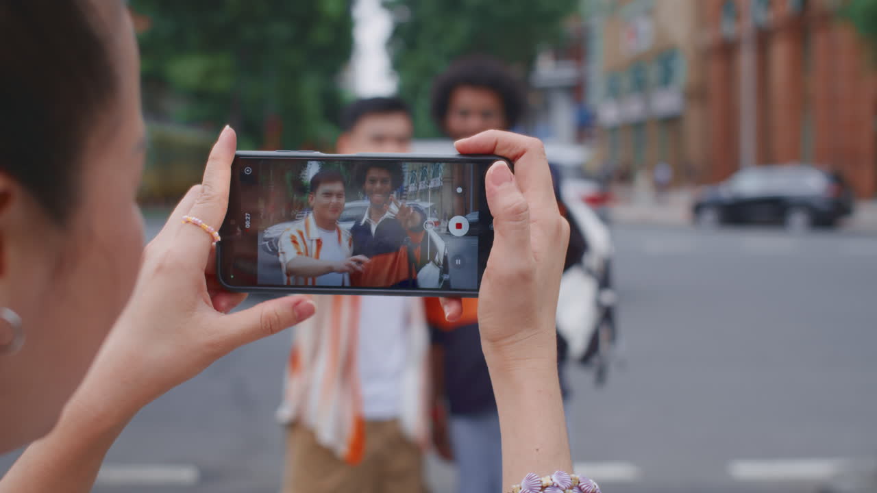 Woman Holding Smartphone to Take Photo of Her Friends Walking in City