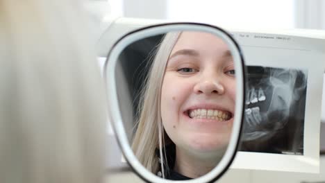 a woman smiles at her teeth in the mirror while in a dentist's office