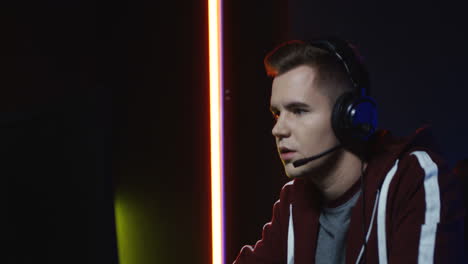 Close-Up-View-Of-Young-Serious-Man-With-Headphones-And-Playing-A-Game-On-The-Computer-In-A-Room-With-Colorful-Neon-Lamps-On-The-Wall-3