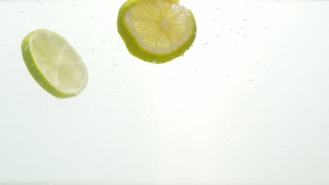rodajas de cítricos verdes cayeron al agua aislado sobre fondo blanco.
