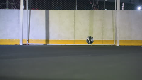 close up of soccer ball being kicked toward goalpost, hitting wall and bouncing back during nighttime on illuminated sports field, capturing motion, energy, and the dynamic