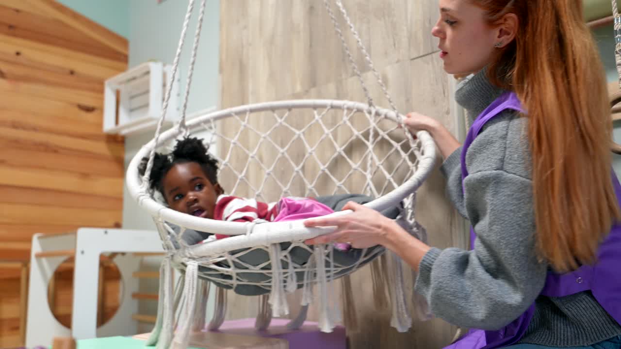 Terapista dondola delicatamente una bambina su un'altalena sensoriale per terapia