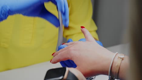 un técnico de uñas, que lleva guantes médicos azules, está limando uñas rojas en la mano de una mujer