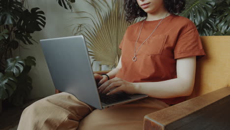 Mujer-Sentada-En-Un-Sillón-Y-Usando-Una-Computadora-Portátil-En-La-Habitación-Con-Plantas