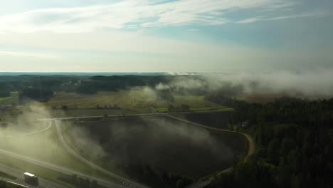 Vista-Aérea-En-Movimiento-Hacia-Atrás-De-La-Niebla-Matutina-Flotando-Sobre-Una-Carretera-De-4-Carriles-Con-Automóviles-Y-Camiones