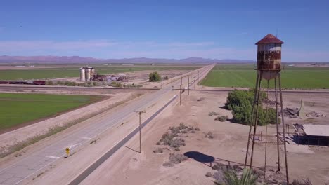 A-high-angle-aerial-over-a-lonely-abandoned-road-through-a-rural-area-with-water-tower-foreground