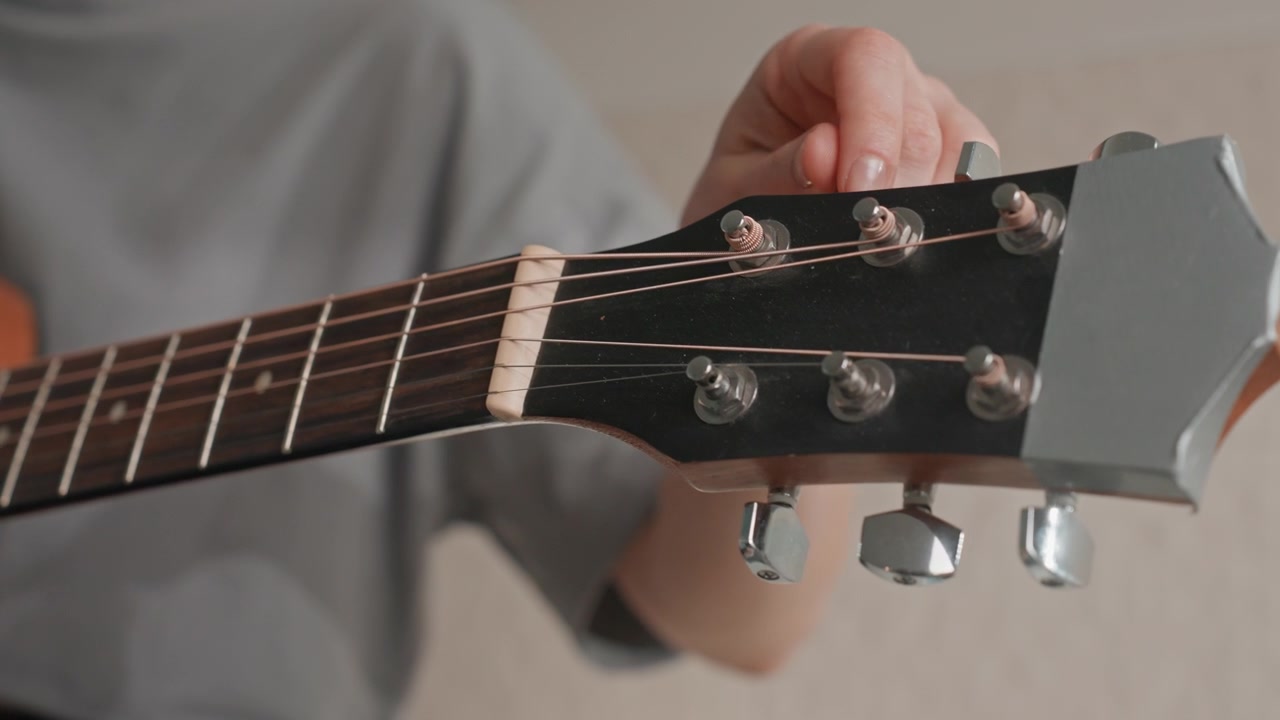 Caucasian woman tuning guitar headstock closeup, fingers adjusting pegs with careful focus, indoor home practice, warm wood tones and metal tuners, concentrated musician preparing song, soft natural