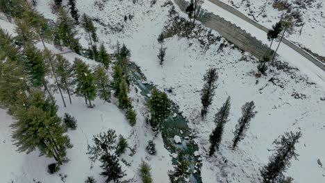 Vista-Aérea-De-Pájaro-Del-Río-Que-Fluye-A-Través-Del-Paisaje-Cubierto-De-Nieve-En-El-Valle-De-Naltar-En-Gilgit