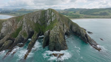 aerial view of rugged, rocky and wild landmass and crashing waves into steep cliffs on the coastline in remote wilderness of cannibal bay, catlins, south island of new zealand aotearoa