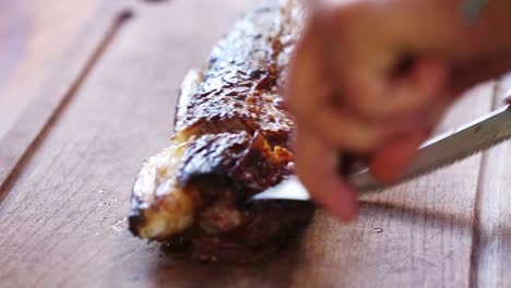 close up view of male hand with a knife slicing a piece of meat on cutting board