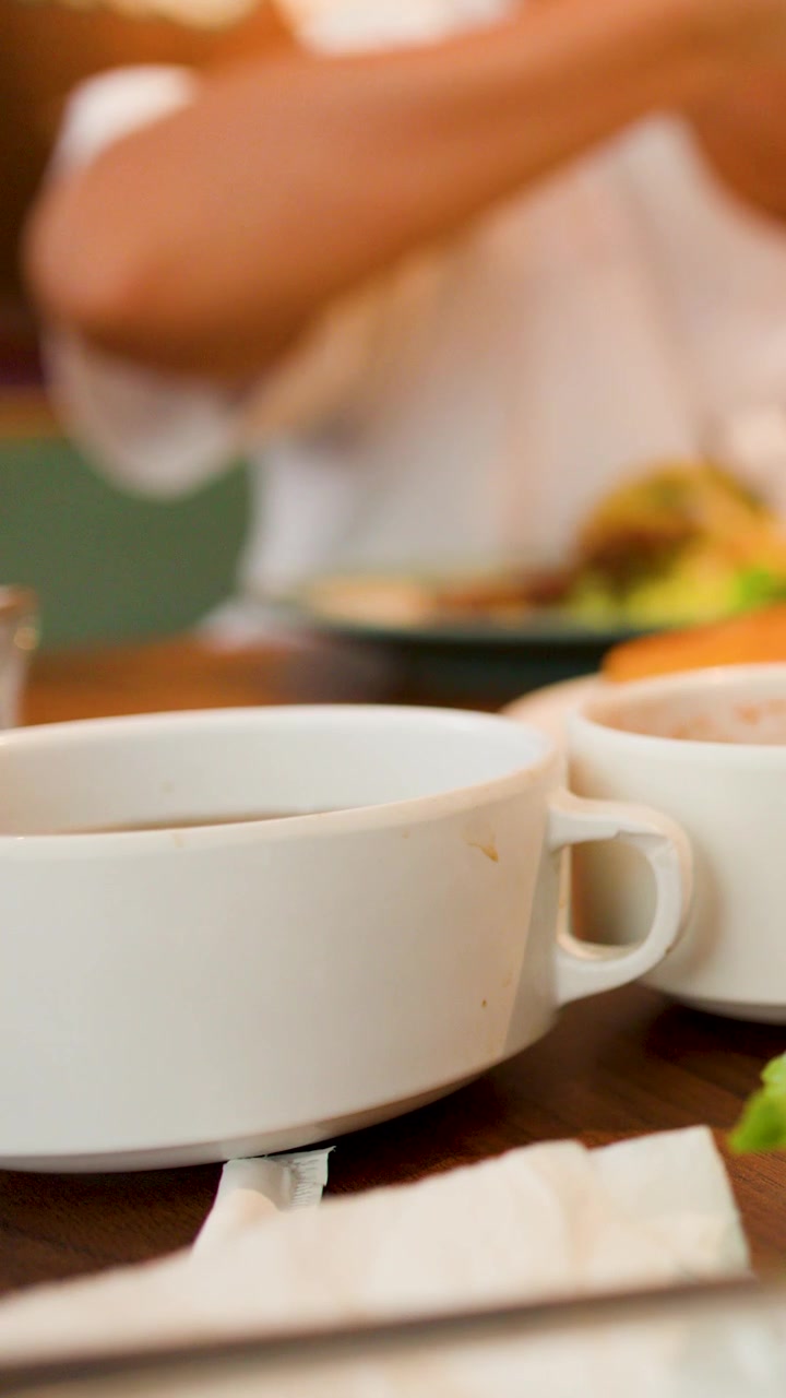 White ceramic soup bowls sit on a wooden table while a person eats in background