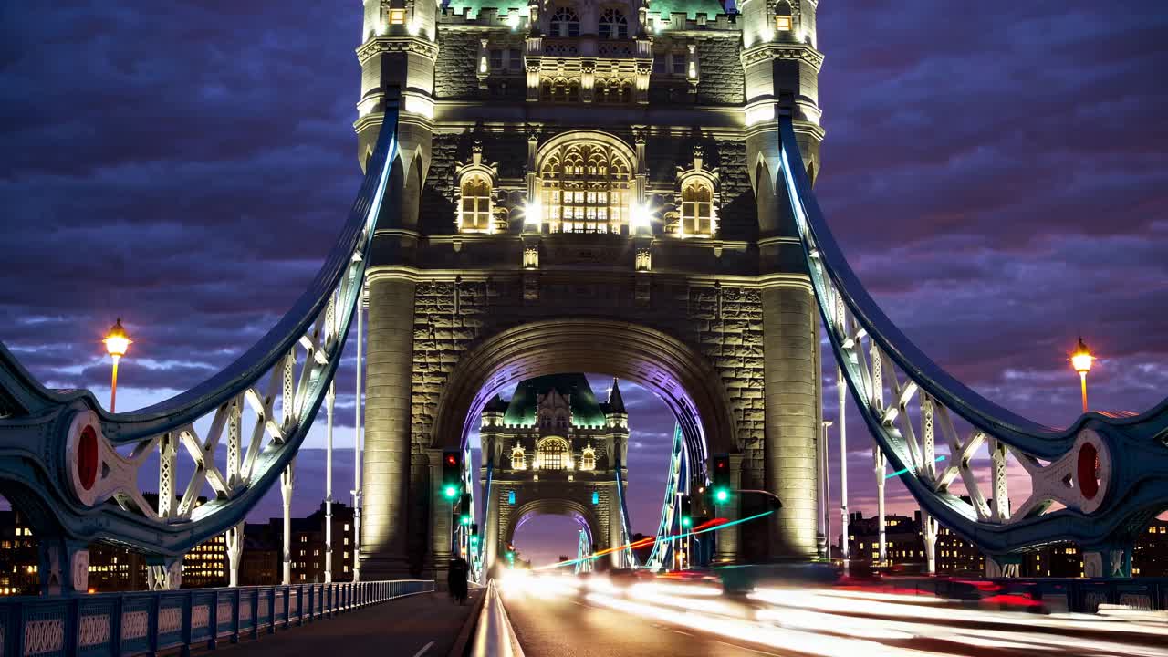 Nighttime video still of a lit-up bridge, captured from a low angle, showcasing dynamic light trails