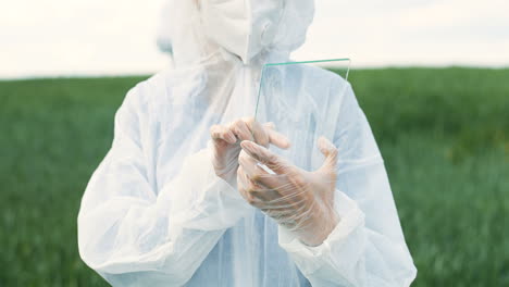 rear view of researcher woman hands in gloves tapping on glass in the green field