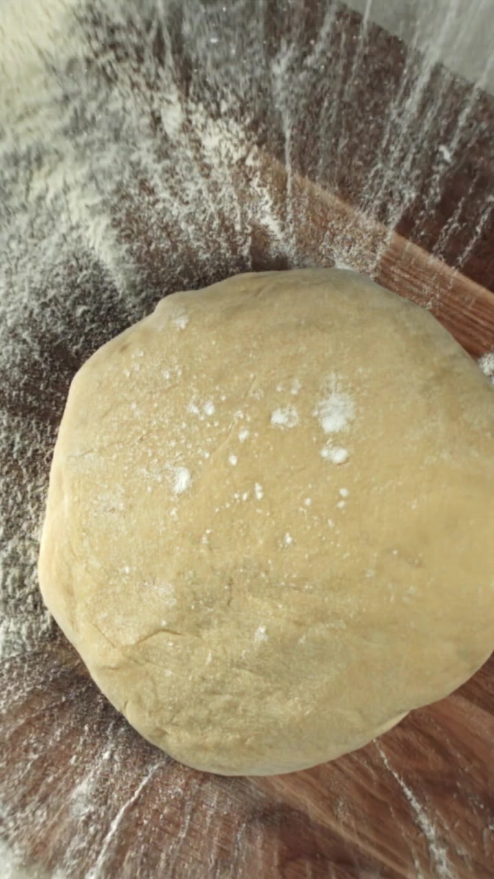 Farina cosparsa attorno a una palla di impasto su una superficie di legno