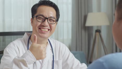 close up of asian male doctor smiling and showing thumbs up gesture to camera while sitting at desk with a fat male patient in clinic