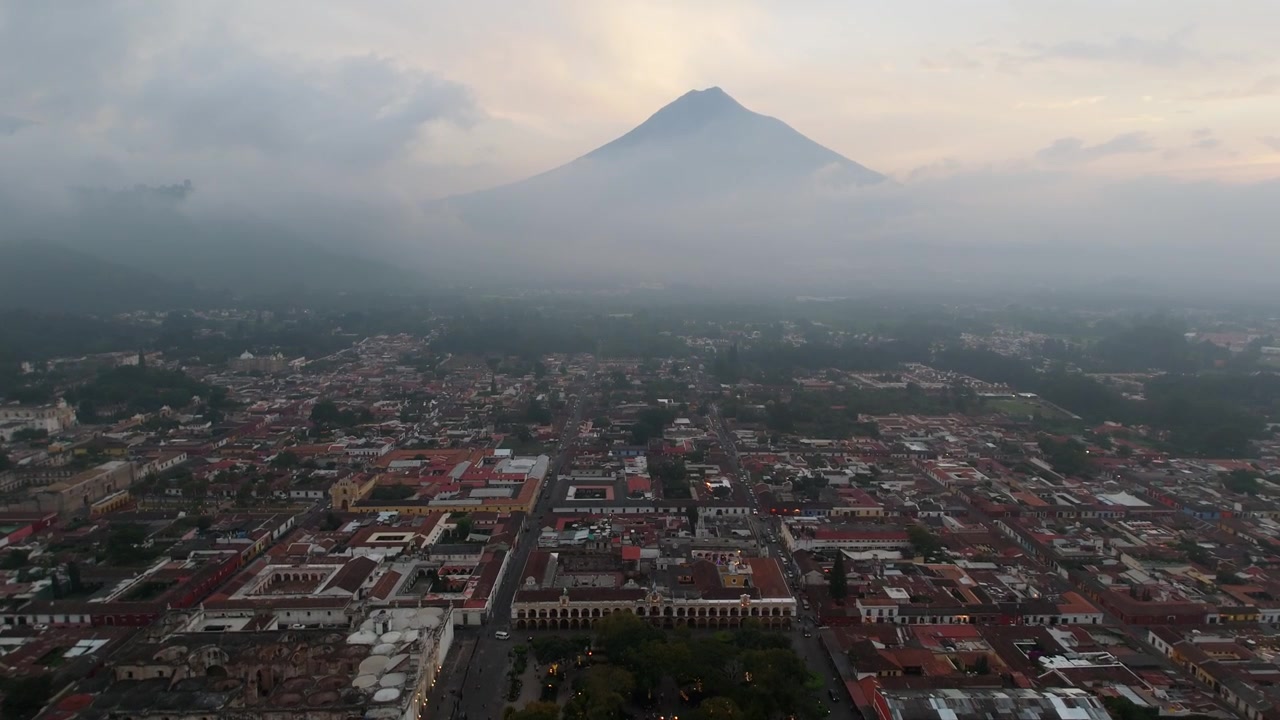 Majestætisk luftperspektiv af Antigua, Guatemala, der afslører den ikoniske Agua-vulkan gennem skyerne.