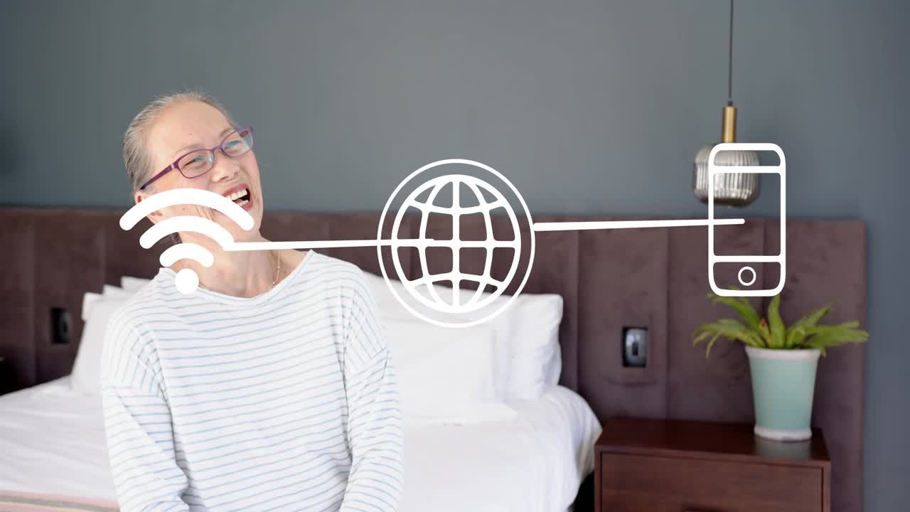 Senior woman sitting in bedroom overlay popping Wi?Fi phone icons dot lit turning laughing to tech