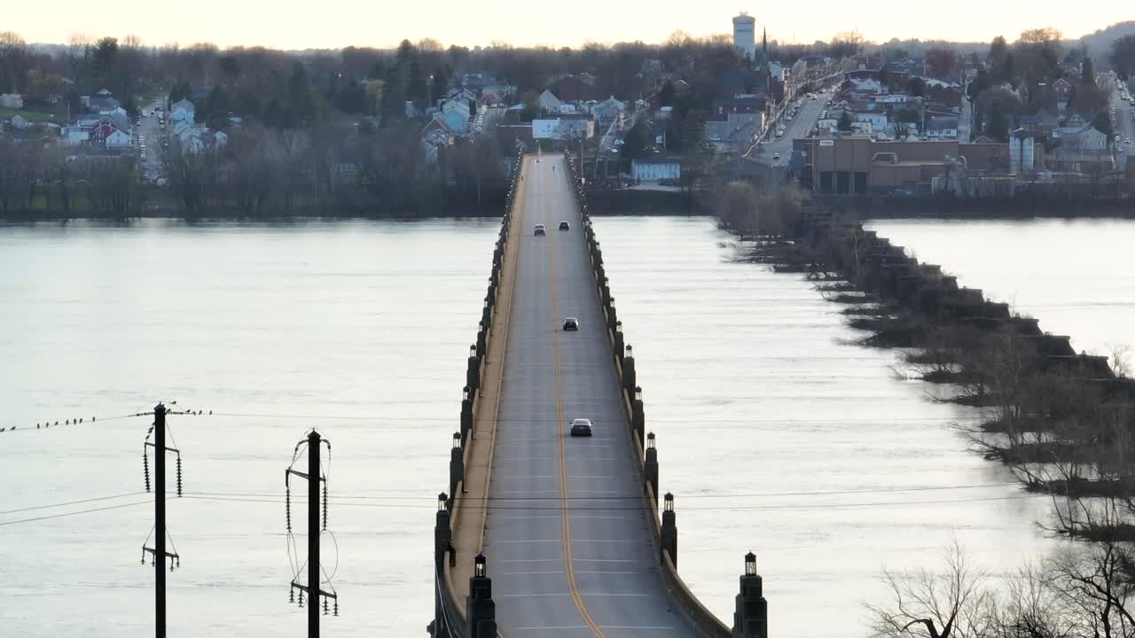 vista de drones de vehículos que conducen por un puente de dos carriles que conduce a un distrito del centro de la ciudad durante la puesta de sol en la primavera