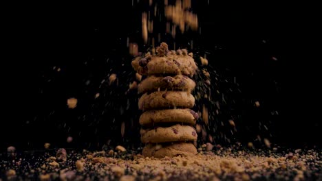 stack of vegan chocolate cookies with biscuit crumbs falling on them while they rotate, slow motion, black background, static shot