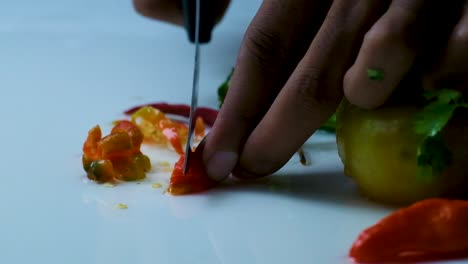 close up cutting bombay chili peppers into small pieces on a white table with other vegetables on the side