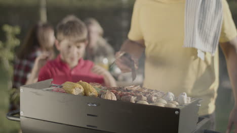 Man-turning-over-meat-on-barbecue-grill,-his-son-blowing-fire