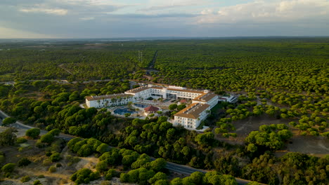 Antenne---Drohne-Nähert-Sich-Langsam-Dem-Luxusgarten-Playanatural-Hotel,-Umgeben-Von-Dichtem-Immergrünen-Steinkiefernwald-Bei-Sonnenuntergang,-El-Rompido,-Andalusien-Skyline,-Spanien