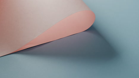 close up of pink rolled paper on blue background with shadow and copy space, in slow motion