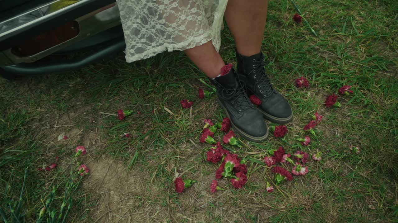 Woman in boots and lace dress next to a car with flowers