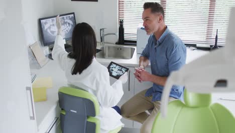 biracial female dentist with face mask examining teeth of male patient at modern dental clinic