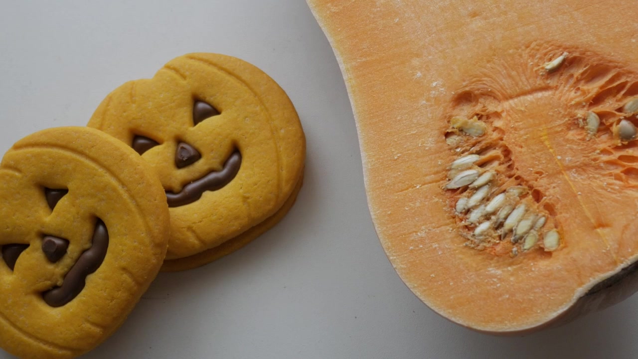 Biscotti a tema Halloween accanto a una zucca butternut fresca su sfondo bianco, primo piano