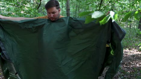 slow motion of a tourist folding a tent at forest campsite and packing up to leave