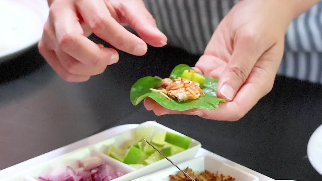 Hands skillfully prepare leaf wraps using fresh ingredients like peanuts, onions, and chili.