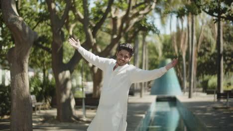 hombre musulmán feliz con camisa blanca levantando las manos en el parque.