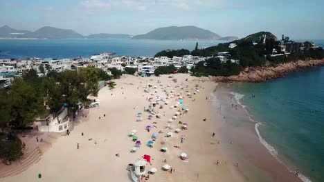una vista aérea en movimiento de los visitantes usando sombrillas en la playa shek o en hong kong mientras las playas públicas reabren al público, después de meses de cierre en medio del brote de coronavirus