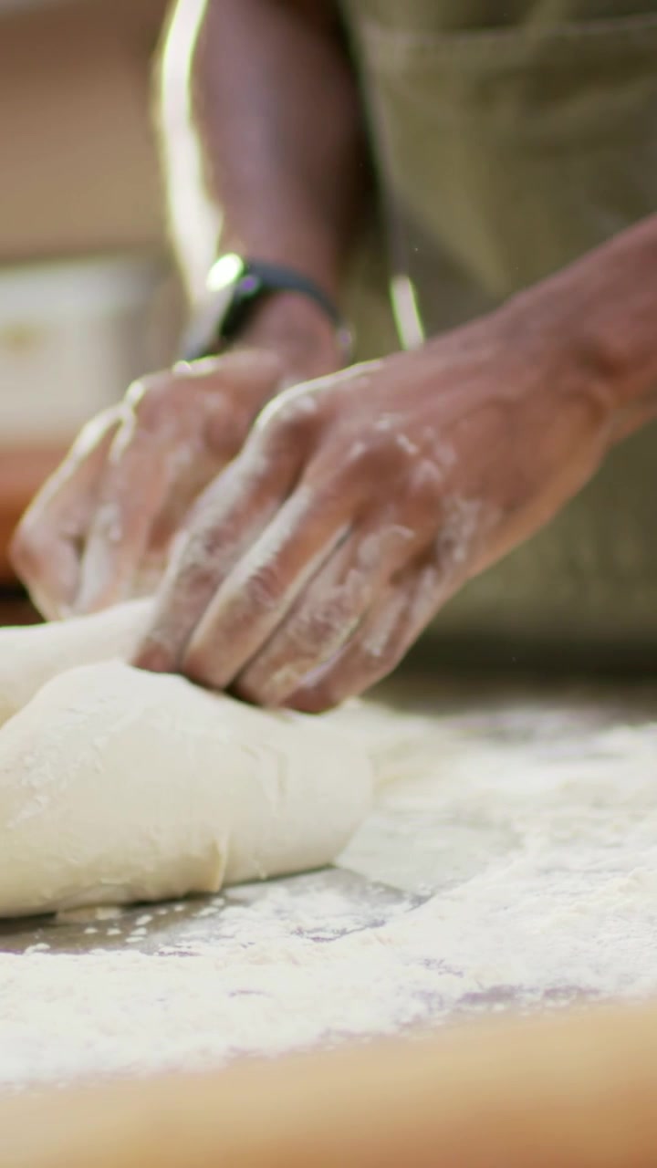 Vertical video: Starting closeup baker hands in apron pressing dough on counter to form boule, jar