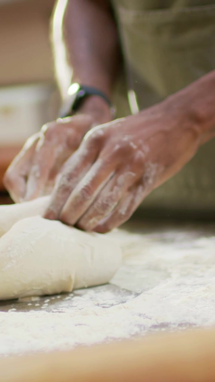 Vertical video: Starting closeup baker hands in apron pressing dough on counter to form boule, jar