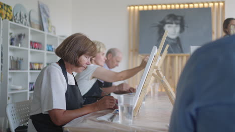 the teacher shows a group of friends of retired people in the elderly at drawing courses. a group of elderly men and women draw together and smile