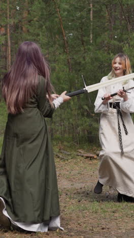 teenagers from middle ages play with swords in century forest, girls in historical dresses