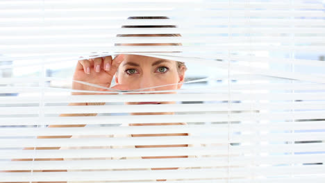 una mujer de negocios fruncida mirando a través de las persianas.
