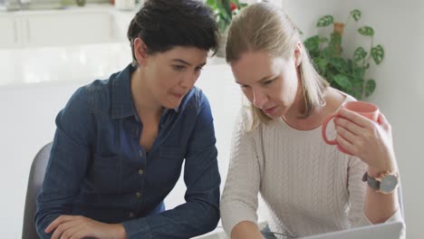 caucasian lesbian couple smiling while talking to each other at home