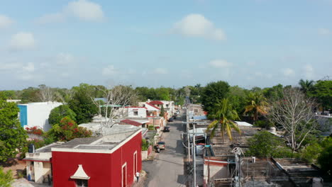 Forwards-fly-above-street-in-suburban-in-tropical-area.-Various-houses-along-road-with-cars-parked-on-side.-Valladolid,-Mexico