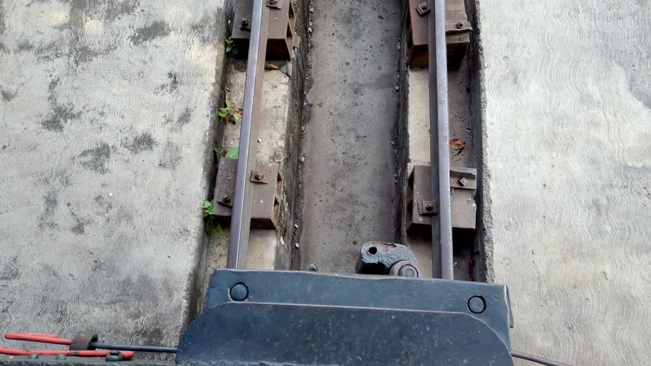 Camera advancing over an old chain mechanism and metal structure near train tracks, cinematic daylight and texture detail