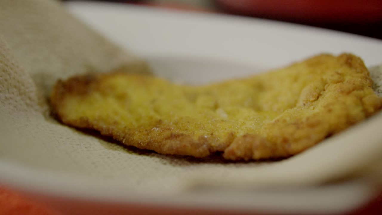 Primo piano di filetto di pollo fritto con panatura croccante e dorata servito su un piatto, cibo appena cucinato, consistenza croccante, preparazione di un pasto delizioso, concetto di comfort food