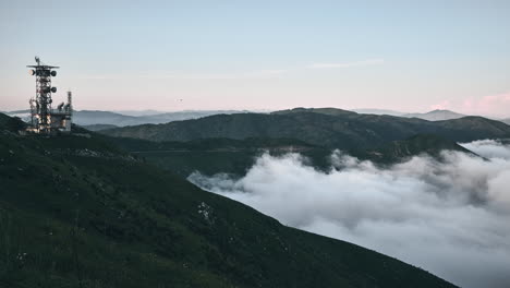 Las-Nubes-Fluyen-Sobre-Los-Picos-De-Las-Montañas-Al-Atardecer-Con-Una-Torre-De-Comunicación,-Timelapse