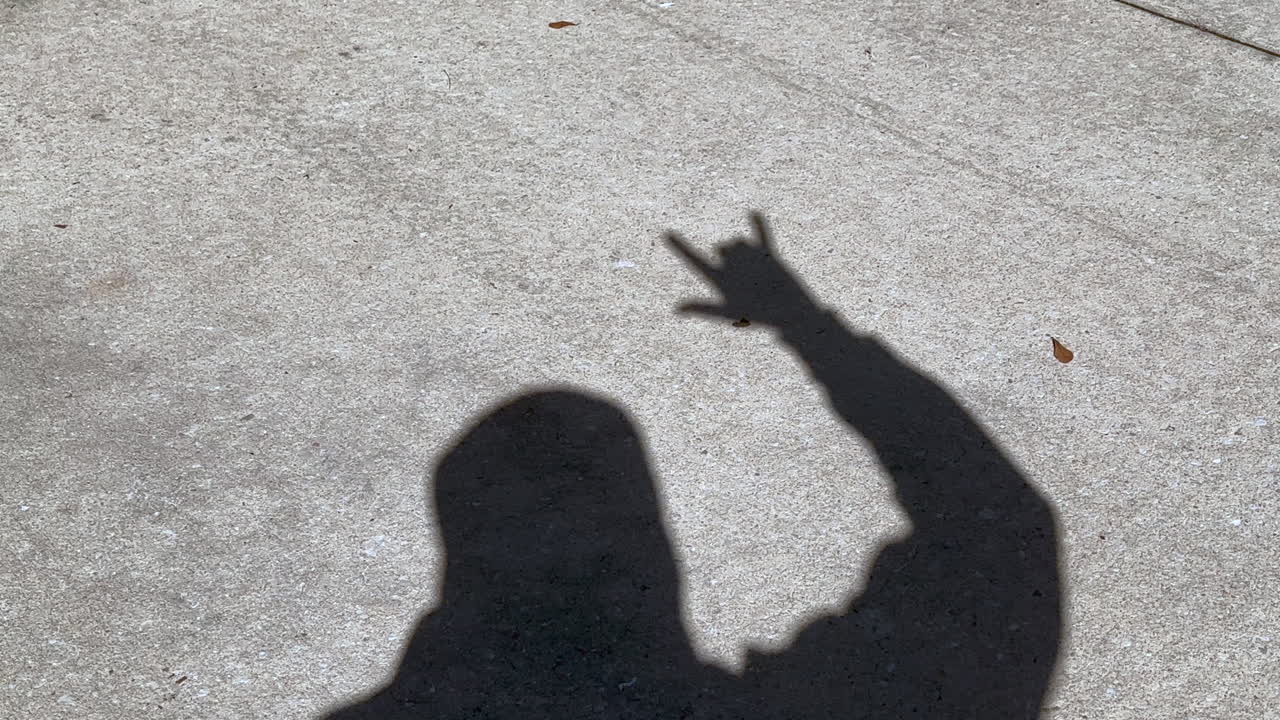 Shadow of man waving rock and roll and rock on sign with fingers on hand