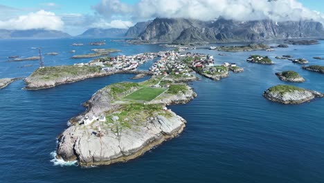 Aerial arc looking down on iconic soccer pitch, Henningsvaer Stadium on Hellandsyya Island, Norway, surrounded smaller Lofoten Islands