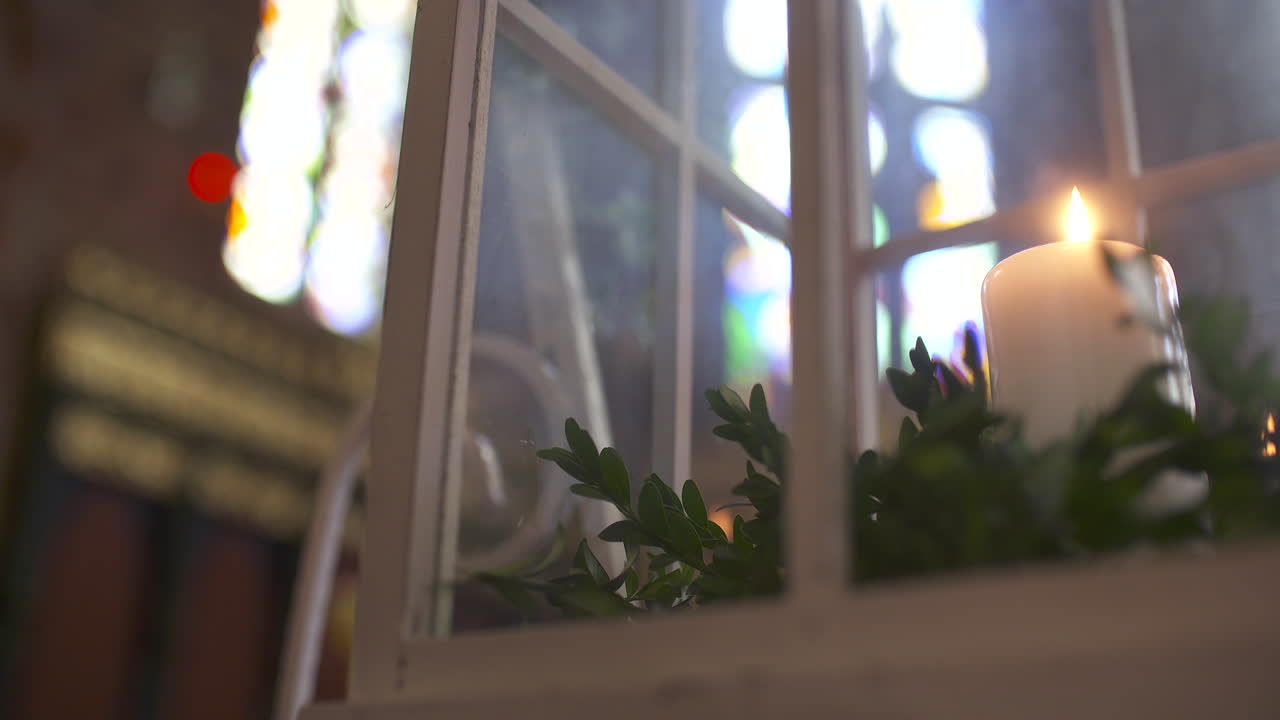 Burning Candle with Greenery in Front of Stained Glass Window