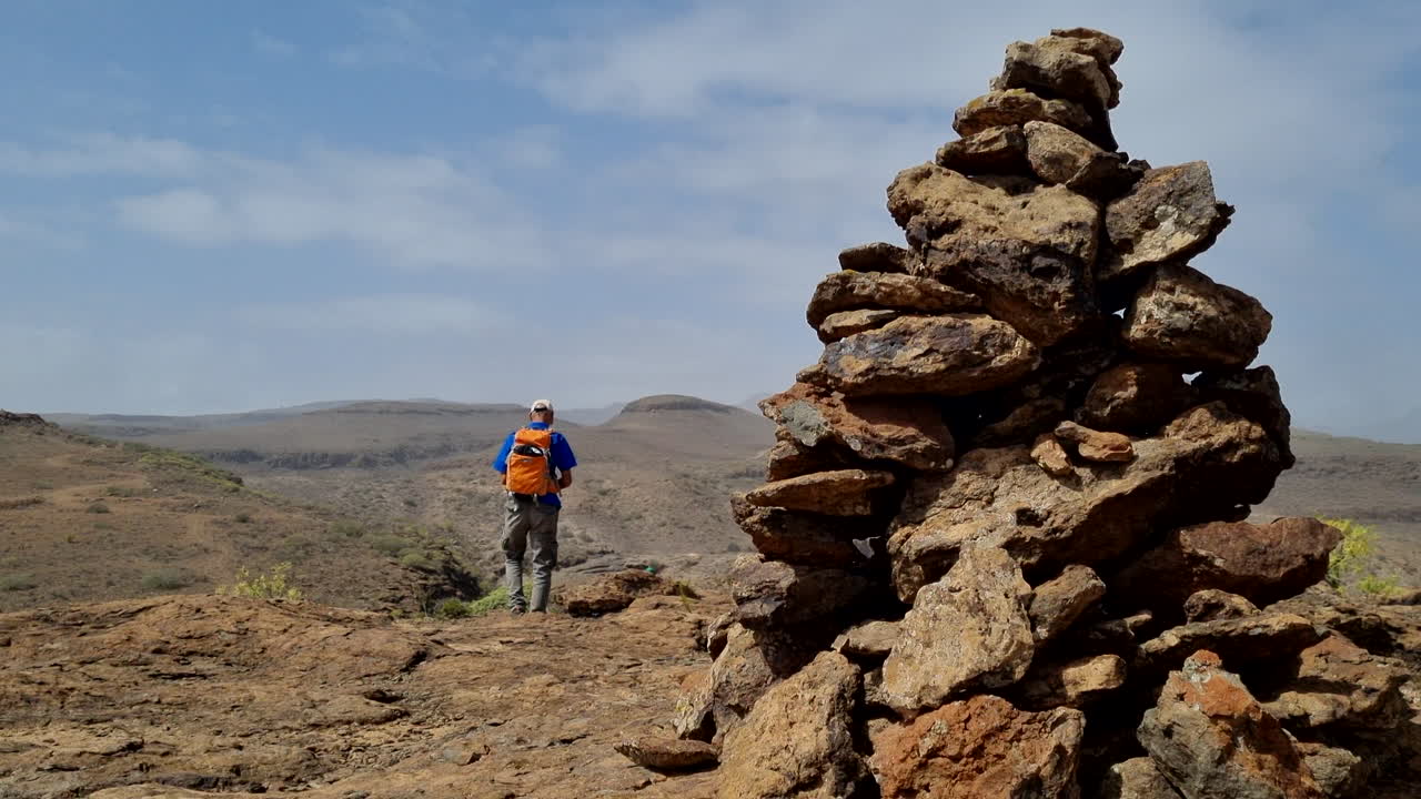 hombre caminando y en primer plano hay un montículo de piedras