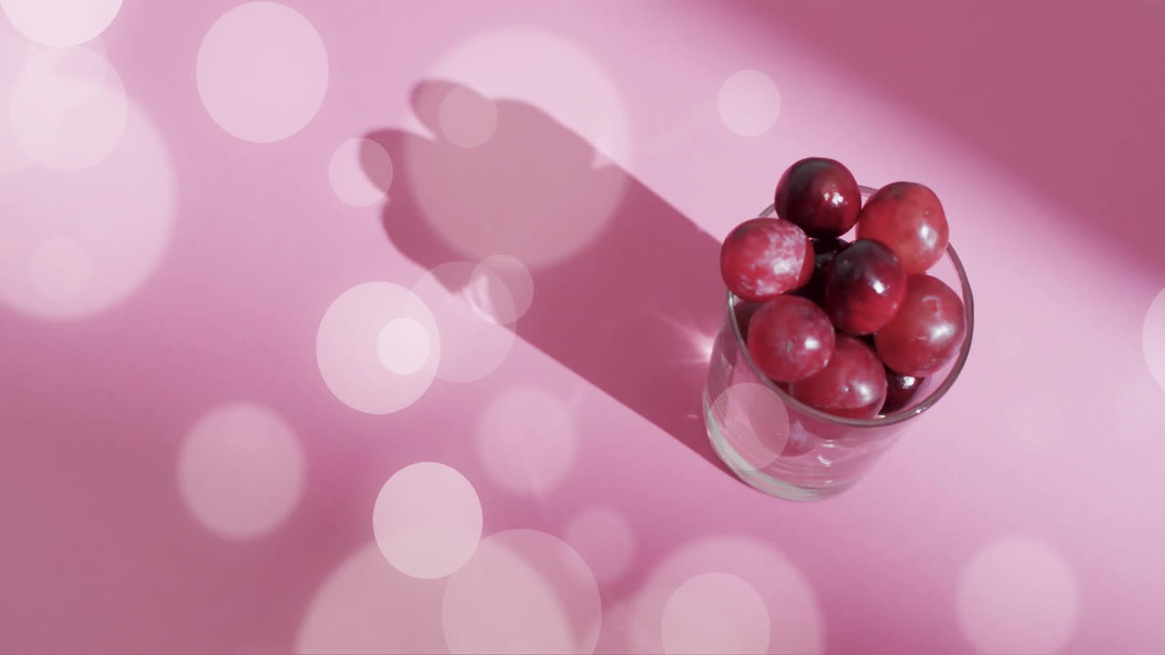 composición de manchas de luz sobre vidrio con uvas rojas sobre fondo rosa
