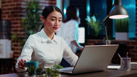 Businesswoman-drinking-coffee-while-doing-tasks-in-office-overnight